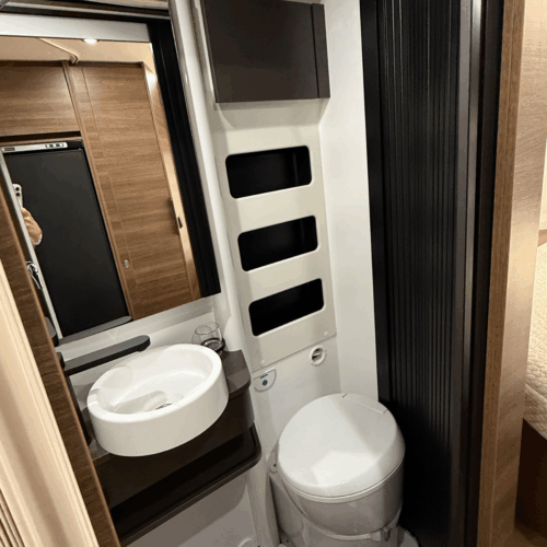 Compact bathroom in the Rapido V64 campervan with cassette toilet, round sink and mirrored storage cabinet.