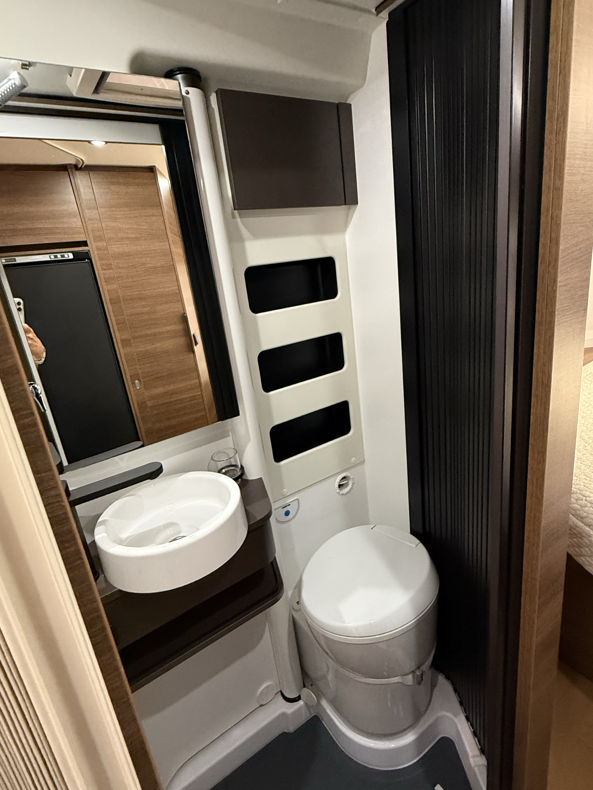 Compact bathroom in the Rapido V64 campervan with cassette toilet, round sink and mirrored storage cabinet.