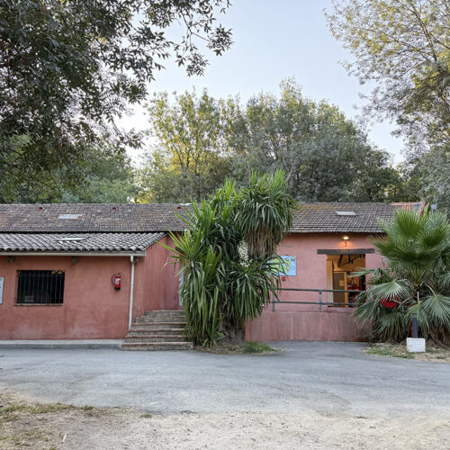 Sanitary building at Camping Parc Bellevue Cannes, pink facade with tiled roof surrounded by palm trees