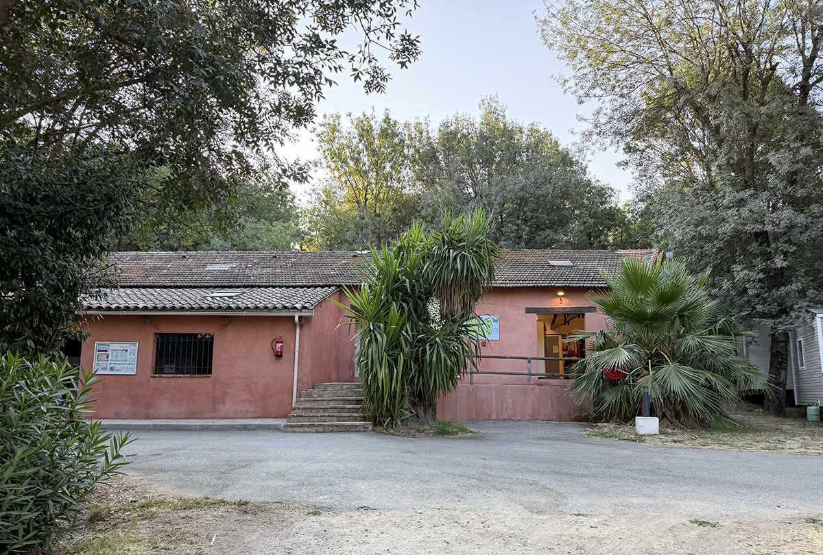 Sanitary building at Camping Parc Bellevue Cannes, pink facade with tiled roof surrounded by palm trees
