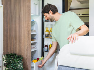 Man reaching into a Thetford 12V compressor fridge in a motorhome, selecting fresh vegetables from the door bin.
