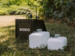 Boxio XL portable washbasin unit with foldable tap and two white water canisters set up outdoors on grass.