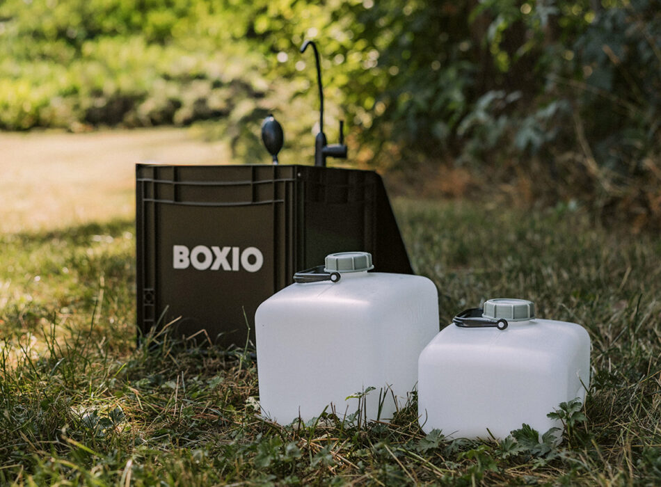 Boxio XL portable washbasin unit with foldable tap and two white water canisters set up outdoors on grass.
