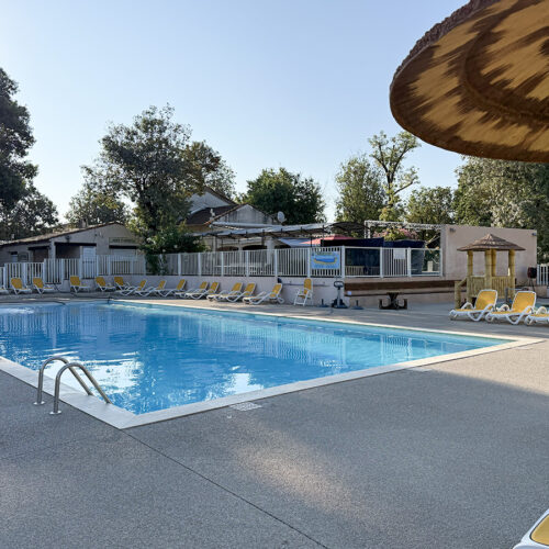 Swimming pool with sun loungers at Camping Parc Bellevue Cannes, surrounded by trees and a straw parasol.