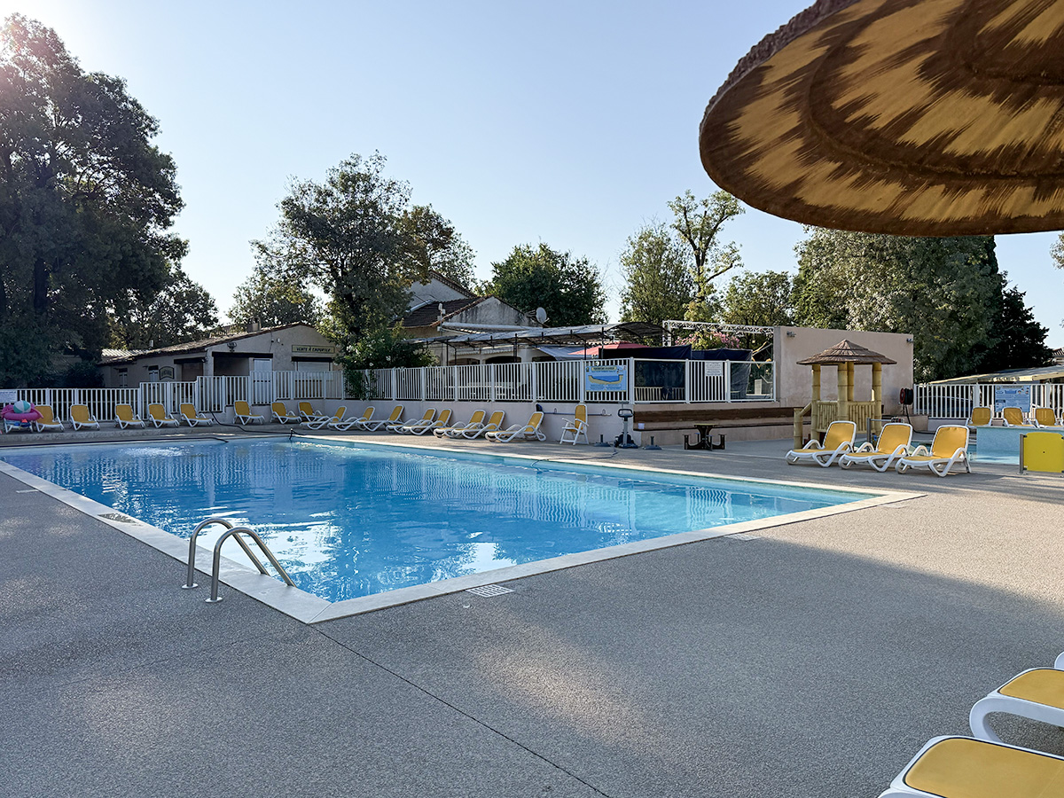 Swimming pool with sun loungers at Camping Parc Bellevue Cannes, surrounded by trees and a straw parasol.