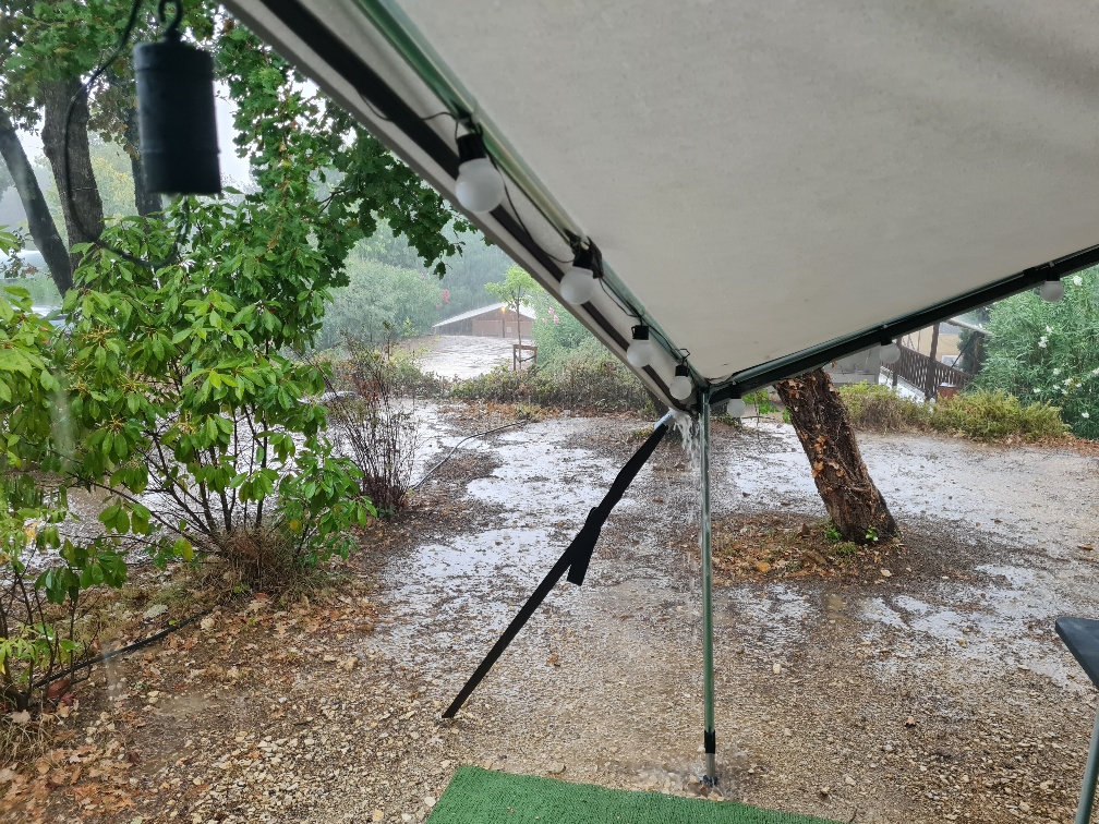 Rainwater streaming off a wet canopy tent onto gravel, highlighting the challenge of packing a wet tent after heavy rain.