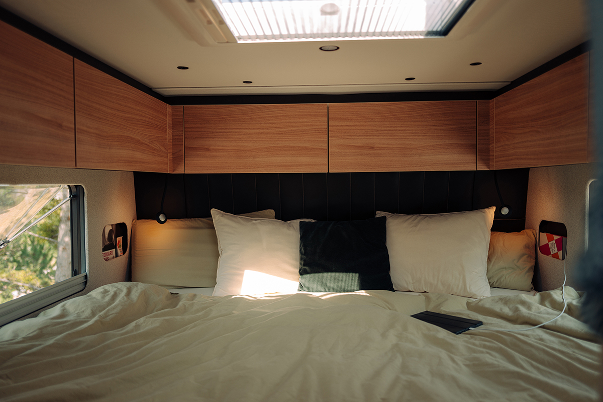Bürstner Signature Mercedes motorhome bedroom with skylight, wooden overhead cabinets and plump white pillows