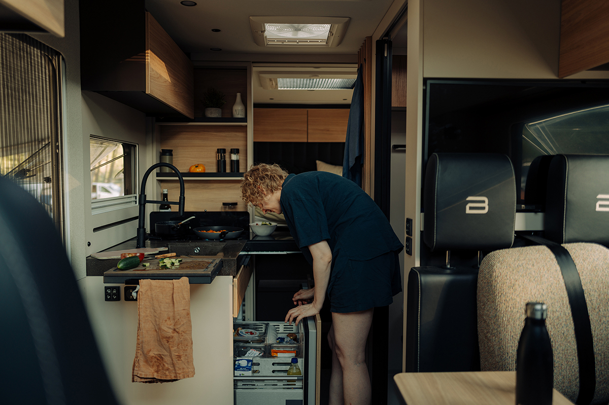 Bürstner Signature Mercedes motorhome kitchen with person reaching into fridge drawer beside hob and worktop