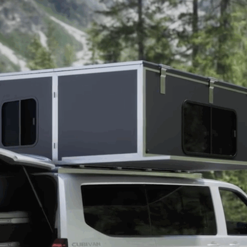 Cubivan camper van with expanded rooftop pop-up cabin featuring windows, parked against a forested mountain backdrop.