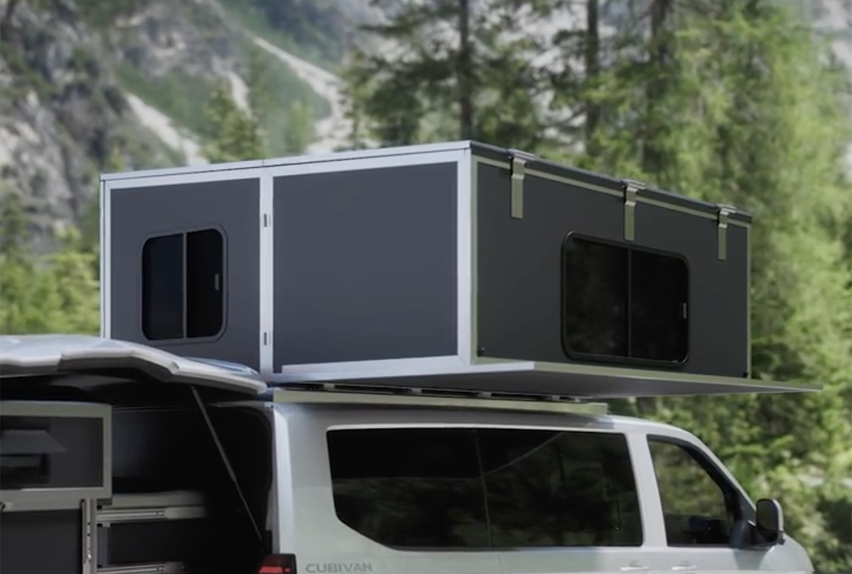 Cubivan camper van with expanded rooftop pop-up cabin featuring windows, parked against a forested mountain backdrop.