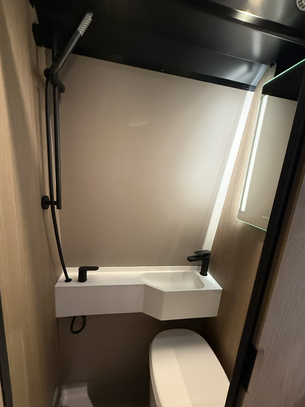 Compact wet room bathroom in the Dovra RIG X-710 with black fittings, handheld shower, white basin and toilet.
