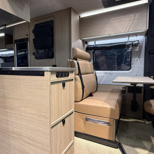 Dovra RIG X-710 campervan interior with kitchenette, swivel seats, fold-out table and wine glass holders.