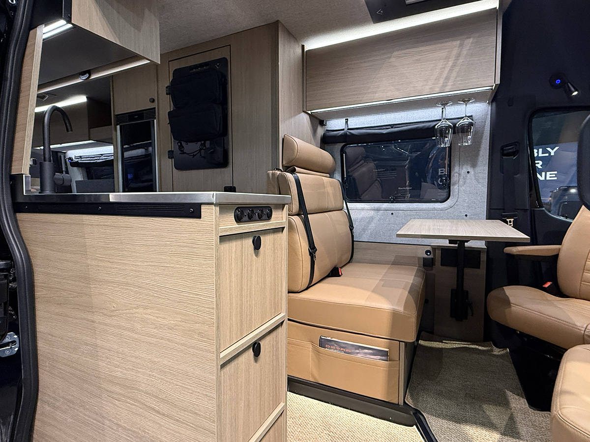 Dovra RIG X-710 campervan interior with kitchenette, swivel seats, fold-out table and wine glass holders.