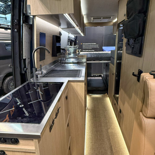 Dovra RIG X-710 camper van kitchen with induction hob, steel sink and ambient LED-lit hallway to rear bed.