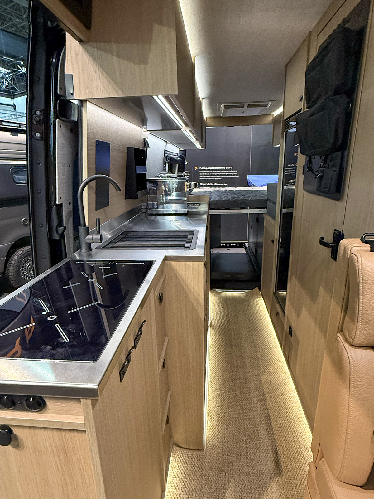 Dovra RIG X-710 camper van kitchen with induction hob, steel sink and ambient LED-lit hallway to rear bed.