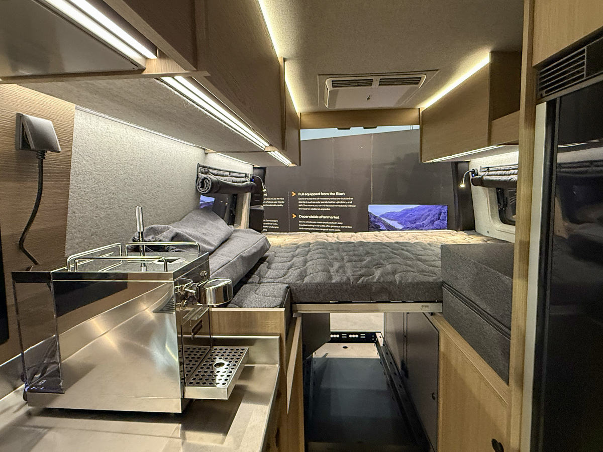 Dovra RIG X-710 campervan interior showing rear bed, overhead cabinets and built-in coffee machine on worktop.
