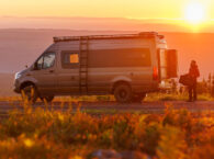 Dovra RIG X-710 camper van parked at sunset, rear doors open, man unloading gear from storage compartment
