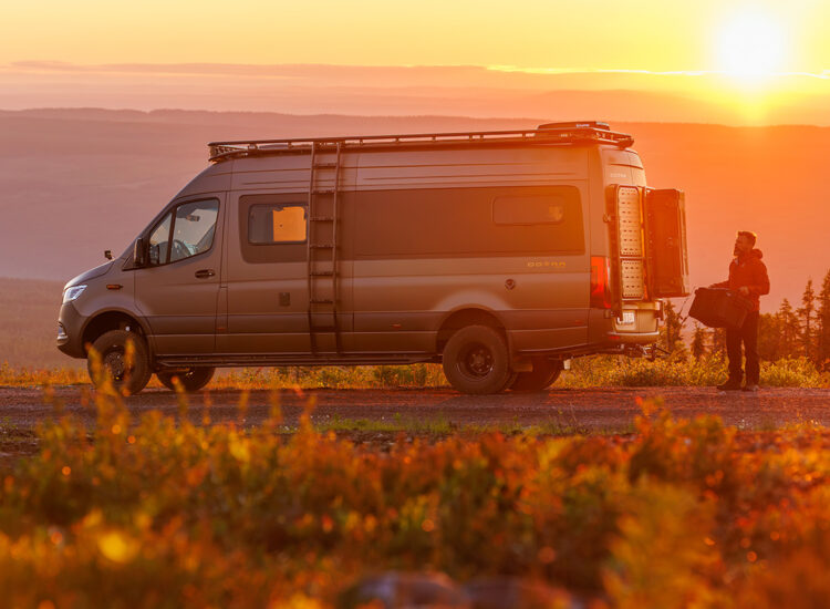 Dovra RIG X-710 camper van parked at sunset, rear doors open, man unloading gear from storage compartment