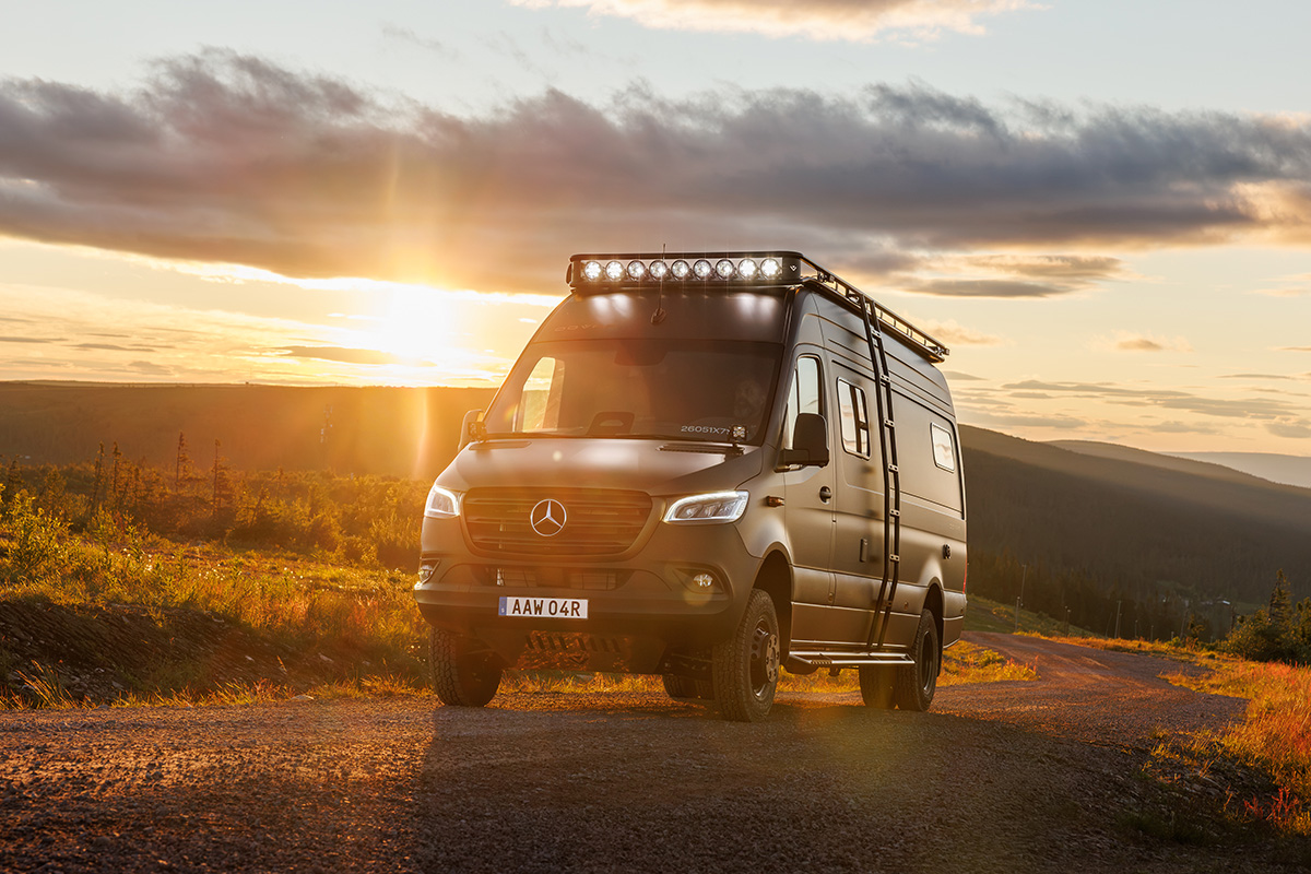Dovra RIG X-710 Mercedes Sprinter camper van on gravel road at sunset with roof light bar and rack