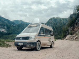 Carado CV595 X-Edition 4x4 campervan driving on a gravel mountain road surrounded by forested peaks