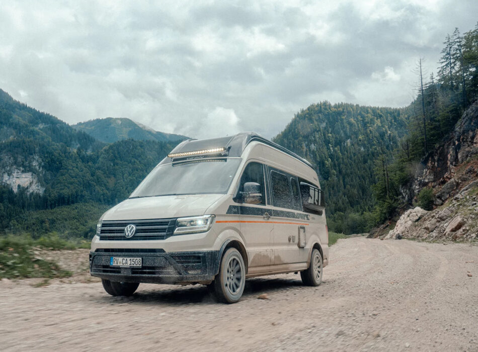 Carado CV595 X-Edition 4x4 campervan driving on a gravel mountain road surrounded by forested peaks