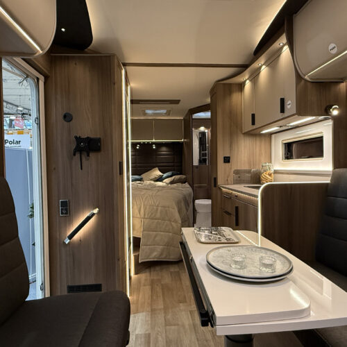 Interior of the Kabe Novum Compact 720 LXL motorhome, showing lounge, kitchen and bed area with wood-finish cabinetry.