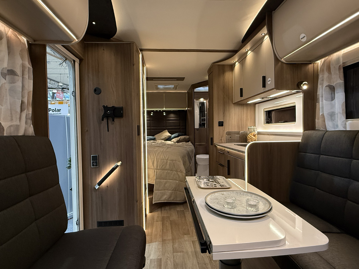 Interior of the Kabe Novum Compact 720 LXL motorhome, showing lounge, kitchen and bed area with wood-finish cabinetry.