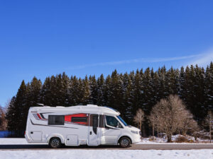 Kabe Novum Compact 720 LXL motorhome parked on a snowy road beside a pine forest under a clear blue sky