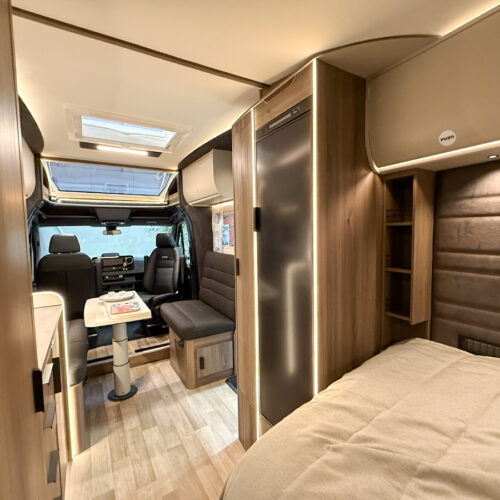 Kabe Novum Compact 720 LXL motorhome interior showing bed, driving cab, dinette and wood-finish cabinetry