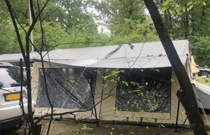 Wet canvas porch tent with mesh windows at campsite, illustrating packing a wet tent after rain in Netherlands.