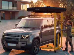 Roof Space rooftop tent hoist lifting a black tent onto a Land Rover Defender using a yellow mobile frame