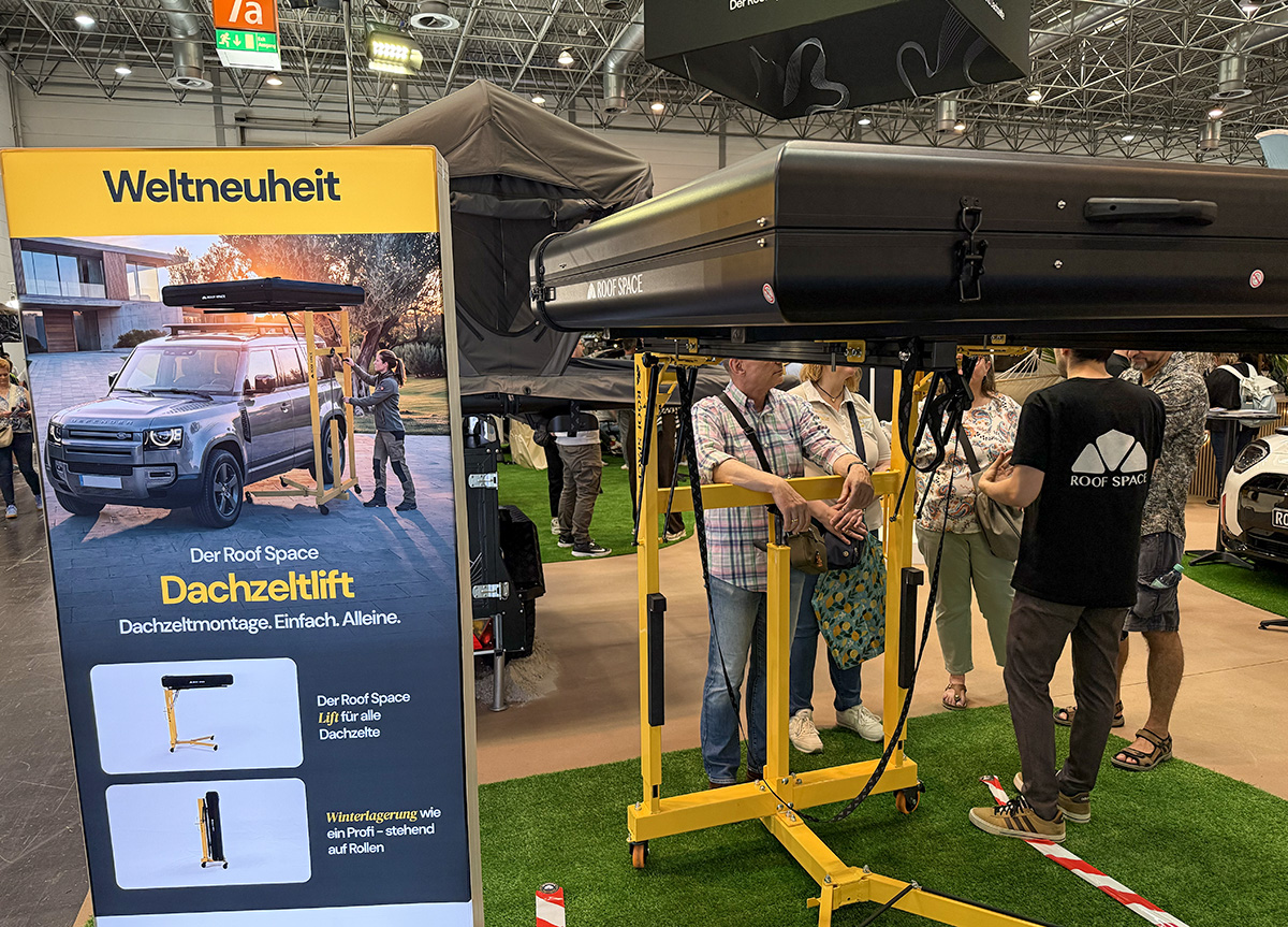 Roof Space rooftop tent hoist on yellow lift stand at Caravan Salon trade show display with demo banner