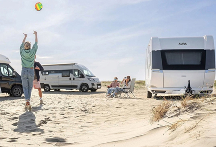 Hobby Aura caravan and motorhome parked on sandy beach with people relaxing and playing with a ball