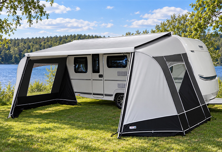 Fendt caravan with Unico Modena cassette awning walls featuring mesh window panel, pitched beside a lake.